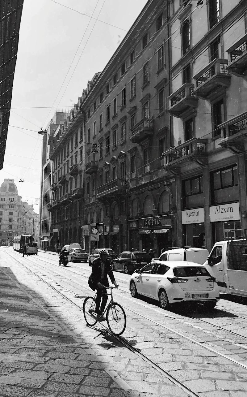 Cars and a cyclist on a cobbled tram street in central Milan